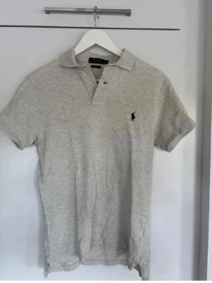 Ljusbeige pikétröja från Polo Ralph Lauren - Säljer en ljusbeige pikétröja från Polo Ralph Lauren i slim fit-modell. Tröjan har korta ärmar, klassisk krage och knappar framtill. Tillverkad i mjuk bomull och har den ikoniska broderade loggan på bröstet.