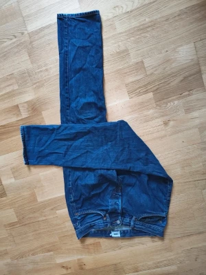 Blå raka jeans med orange sömmar - Säljer ett par klassiska blå jeans med raka ben och snygga orange sömmar. Jeansen har fem fickor och stängs med dragkedja och knapp. Perfekta till vardagslooken och passar till det mesta i garderoben.