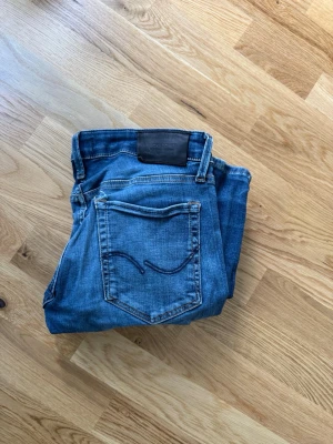 Jack and Jones jeans slim fit - Snygga blå jeans i slim fit-modell med klassisk femficksdesign och markerad bakficka med broderad detalj. Jeansen har normal midja och är tillverkade i denim med lätt tvättad look. Perfekta för en avslappnad och trendig stil. Skriv om ni har några frågor. Stl 27 men de är stretchiga så passar upp till 30. Finns hål här och där