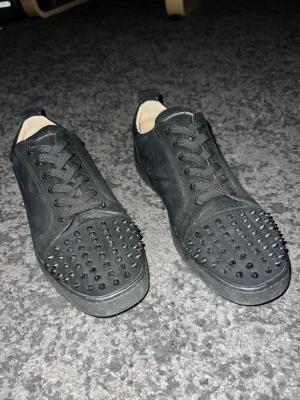 Svarta loubs med röd sula - Säljer ett par svarta loubs som är nytvättade och endast använde 10-20gånger. Skorna har snörning och är gjorda i mockaliknande material med en låg siluett. Insidan är ljus och sulan är svart. Perfekta för dig som vill sticka ut med din stil.