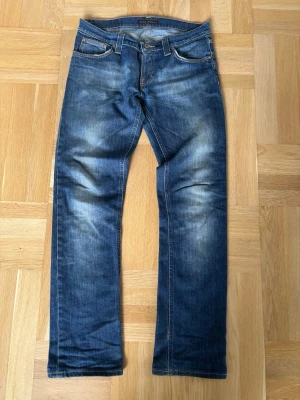 Blå jeans från Nudie Jeans - Säljer ett par klassiska blå jeans från Nudie Jeans med något slimmade ben . Jeansen har fem fickor, bälteshällor och dragkedjegylf. Perfekta för en avslappnad och trendig look. Något lågmidjade. 