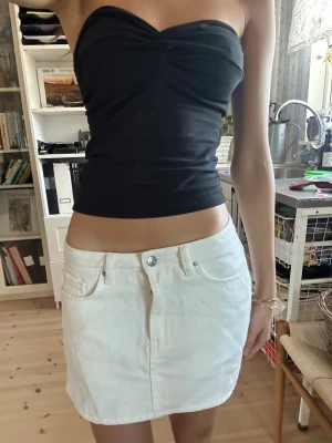 Vit kortkjol  - Snygg vit kortkjol i denim med klassisk femficksdesign och knappstängning fram. Kjolen har en enkel och stilren look som passar till många olika outfits. Perfekt för dig som gillar en fräsch och clean stil.