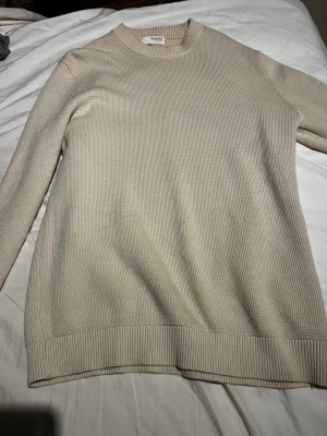 Beige stickad tröja från Selected Homme - Snygg beige stickad tröja från Selected Homme med rund halsringning och ribbade muddar vid ärmslut och nederkant. Knappt använd, inprincip som ny