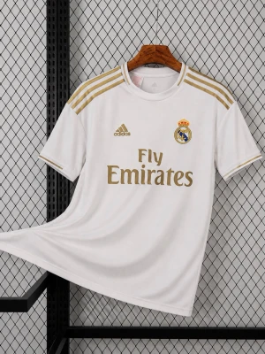 Real Madrid matchtröja Adidas - Säljer en vit Real Madrid matchtröja från Adidas med gulddetaljer och klubbmärke på bröstet. Tröjan har korta ärmar, rund hals och tre guldiga ränder på axlarna. Tryck med 'Fly Emirates' fram och 'Vinicius Jr. 25' bak. Perfekt för fotbollsfans!
