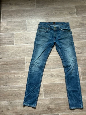 Blå slim fit jeans från Lee - Snygga blå slim fit jeans från Lee med klassisk femficksdesign och slitningar på låren. Jeansen har normal midja, dragkedjegylf och är tillverkade i denim. Perfekta för en avslappnad och trendig look.