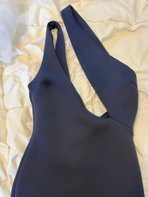 Marinblå oneshoulder klänning - Snygg marinblå klänning med oneshoulder-design och figurnära passform. Kjolen har volangdetalj nedtill som ger extra rörelse och stil. Perfekt för dig som vill sticka ut med en unik och trendig look.