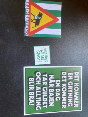 2Hammarby klibbor den i mitten är inte en klibba/klistermärke. - Tre klistermärken med Bajen-tema. Ett med texten 'BAJEN ÖVERALLT' och get i halsduk på grönvit bakgrund, ett litet med handskriven text 'JUST idag ÄR jag STARK', samt ett större grönt med vit text om Bajen och guld. Perfekt för fans av Hammarby.