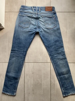 Vintage Replay jeans - Säljer ett par vintage replay anbass jeans med slitningar och hål på låret och knät. Jeansen har klassisk femficksdesign, dragkedjegylf och detaljerade sömmar. Materialet är denim i bomull med stretch för skön passform. Strl:32. - Lagat hål vid grenen.