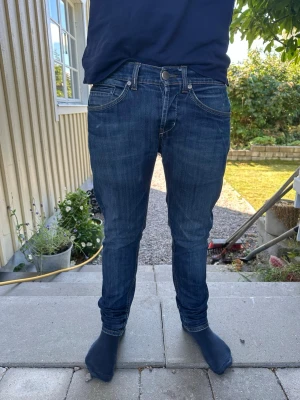 Mörkblå slim fit jeans från Dondup - Säljer ett par mörkblå slim fit jeans med klassiska fem fickor och snygga slitningar. Jeansen har normal midja, smala ben och kontrastsömmar. Perfekta för dig som gillar en modern och stilren look. Materialet är mjukt denim i bomull.