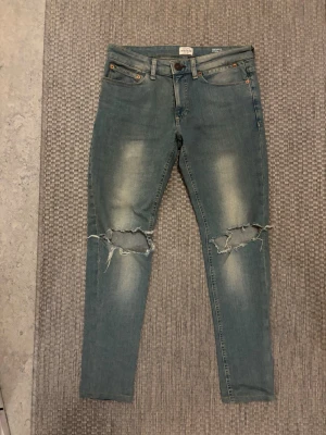 River Island skinny jeans med slitningar - Snygga ljusblå skinny jeans från River Island med stretch och slitna detaljer över knäna. Jeansen har klassisk femficksmodell och är perfekta för en avslappnad streetstil. Materialet är mjukt och följsamt för extra komfort.