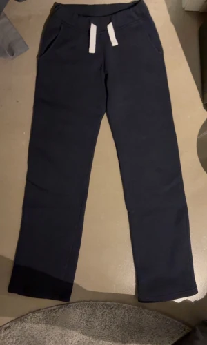 Russemerch byxor - Mörkblå mjukisbyxor med raka ben och vita dragsnören i midjan. Byxorna har två sidofickor och är gjorda i ett mjukt och bekvämt material, perfekta för en avslappnad stil.