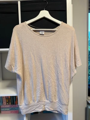 Beige loose topp med kort ärm - En enkel och stilren beige topp med rund halsringning och lös passform. Toppen är kortärmad och sitter löst överallt förutom längst ner där den sitter lite tajtare. Aldrig använt