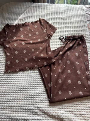 Brunt vardags set  - Fint tvådelat set i brun med vita små blommor och prickar. Setet består av en kortärmad topp med vågig kant som går lite ofshoulder och matchande byxor med stretchig midja. Perfekt för flera ställen och använd ca 3 gånger 🤩