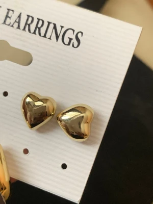 Guldiga hjärtformade örhängen - Snygga örhängen i form av hjärtan med en blank, guldig finish. De är små och stilrena, perfekta för att ge din look en söt touch. Materialet ser ut att vara metall med spegelblank yta. Passar dig som gillar trendiga och klassiska accessoarer.