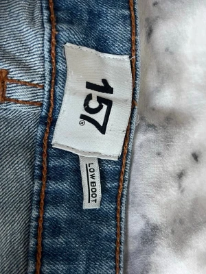 Blå bootcut jeans från Lager 157 - Snygga blå bootcut jeans från 157 med låg midja. Klassisk femficksmodell med orangea sömmar och lätt utsvängda ben. Perfekta för dig som gillar retrovibbar och en avslappnad stil. Tillverkade i denim med en autentisk tvätt.