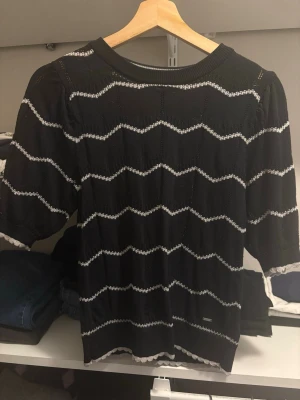 Svart vit randig tröja - Svart  tröja från Holly & Whyte by Lindex med vita sicksack-ränder. Tröjan har rund halsringning, halvlånga ärmar och ribbade kanter. Perfekt för en trendig och avslappnad look. Super fint skick dock lite färg på undersidan som inte syns annars. 
