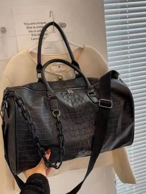 Svart weekendbag i krokopräglat material - Stilren svart weekendbag med krokodilpräglat mönster. Väskan har både handtag och justerbar axelrem samt en dekorativ kedjedetalj på sidan. Perfekt för resor eller gymmet. Dragkedja upptill och rymligt huvudfack.