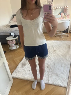 Vit ribbad topp med spetskant - Vit topp med ribbad struktur och söt spetskant runt urringningen. Kortärmad och figurnära modell med lätt v-ringad hals. Perfekt för dig som gillar en feminin och enkel stil.