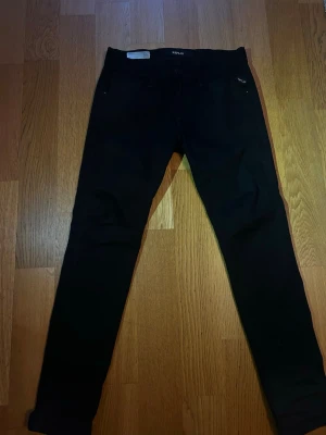 Replay ambass svarta Jeans W29 L30 - Säljer ett par svarta Replay jeans med klassisk femficksdesign och smal passform. Jeansen har normal midja och är tillverkade i ett stretchigt material för extra komfort. Perfekta för en stilren och enkel look.