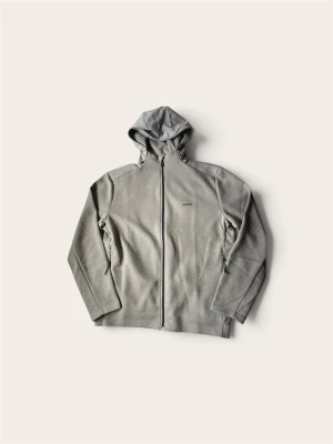 Grå hoodie med dragkedja från BOSS - Stilren grå hoodie från BOSS med hel dragkedja och huva. Diskret BOSS-logga på bröstet och svarta detaljer vid dragkedjan. Tillverkad i mjukt material som känns skönt mot huden. Perfekt för en avslappnad och trendig look.