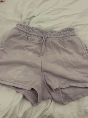 Ljuslila mjukisshorts med snörning - Säljer ett par ljuslila mjukisshorts med elastisk midja och snörning. Shortsen har en avslappnad passform och är tillverkade i mjukt bomullsmaterial, perfekta för varma dagar eller chill hemma. Fickor på sidorna för extra bekvämlighet.