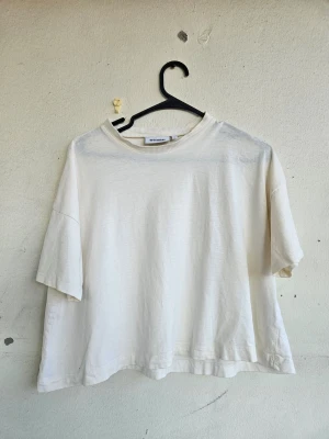 Vit topp från Weekday - Varmvit t-shirt från Weekday med korta ärmar och rund halsringning. Gjord i mjuk bomull. Storlek S. Fint skick!