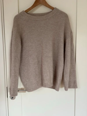 Beige stickad tröja från Lindex - Mysig beige stickad tröja från Lindex i storlek S. Tröjan har en avslappnad passform, rund halsringning och ribbade muddar vid ärmslut och nederkant. Perfekt för lager på lager och enkel att matcha med olika outfits.