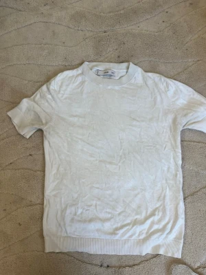 Vit ribbad kortärmad topp - En enkel och stilren vit topp med korta ärmar och ribbade kanter vid hals, ärmslut och nederkant. Passformen är normal och materialet känns mjukt och bekvämt, perfekt till alla dina outfits.