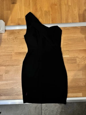 Svart one shoulder klänning Zalando  - Snygg svart klänning med one shoulder-design och figurnära passform. Klänningen har en asymmetrisk axel och stilren look, perfekt för dig som vill sticka ut. Materialet känns mjukt och följsamt mot kroppen.