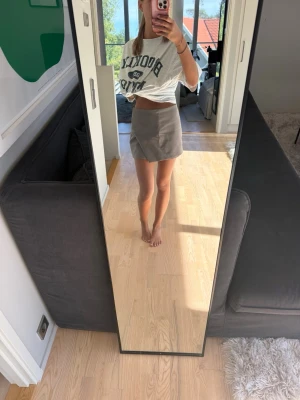 Beige kortkjol i mockaimitation - Säljer en stilren beige kortkjol i mockaimitation. Kjolen har en enkel, rak passform och slits framtill för en trendig look. Perfekt att matcha med en croppad t-shirt eller stickad tröja.