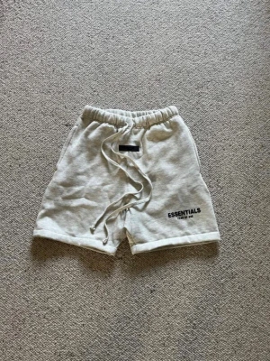 Essentials shorts - Ett par gråa essentials shorts med svart text nere vid vänstra benet. De är i storlek S och i nytt skick. Pris kan diskuteras och skriv om du har några frågor. 
