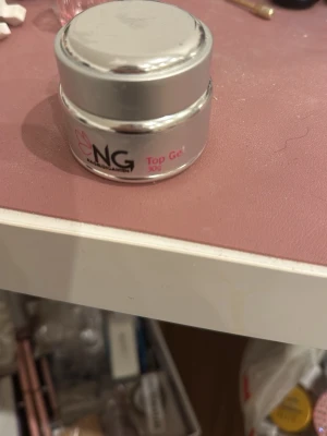 NG Top Gel 30g för naglar - NG Top Gel 30g i en silverfärgad burk, perfekt för att ge naglarna en glansig och hållbar finish. Gelen är genomskinlig och används som sista steg vid gelénaglar för extra glans och skydd. Smidig burk som är enkel att använda vid nagelförlängning eller förstärkning. Endast testad en gång