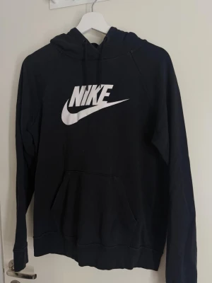 Svart Nike hoodie - Säljer en svart hoodie från Nike med stor vit logga på bröstet. Hoodien har huva med dragsko och en stor magficka. Tillverkad i mjukt material.