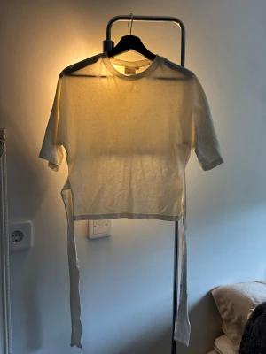 Vit topp med öppen rygg och knytband - Trendig vit topp med korta ärmar och rund hals. Toppen har långa knytband i sidorna som ger en snygg detalj och möjlighet att justera passformen. Perfekt för dig som gillar en enkel men cool stil. Med öppen rygg storlek xxs men passar bra i xs 