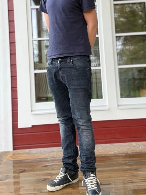 Svarta nudie  slim fit jeans herr - Säljer ett par mörkblå slim fit jeans med lätt slitna detaljer och klassisk femficksmodell. Jeansen har normal midja och smal passform hela vägen ner. Perfekta för dig som gillar en enkel men snygg stil. Det är storlek w32 l32 men passar w30 l32