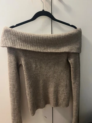 Beige off shoulder stickad tröja H&M - Säljer en beige ribbstickad off shoulder-tröja från H&M. Tröjan har långa ärmar och bred, vikt krage som ger en snygg och trendig look. Perfekt för dig som vill ha något både bekvämt och stilrent till hösten eller vintern.