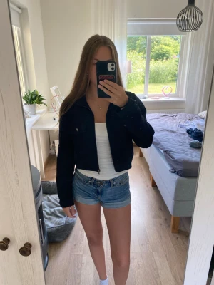 Svart croppad jacka - Snygg svart croppad jacka med dragkedja framtill och långa ärmar. Jackan har en klassisk krage och knappdetaljer vid bröstet. Perfekt för dig som vill ha en stilren och trendig look.