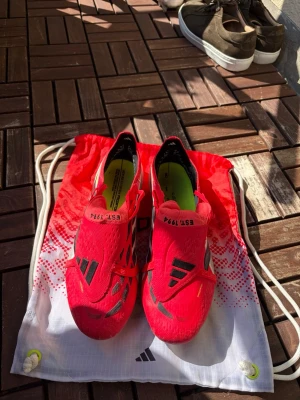 Röda Adidas predator elite med tunga. Fotbollsskor med storlek  45⅓ - Säljer ett par grymt snygga röda Adidas fotbollsskor med svarta och vita detaljer. Skorna har låg profil, snörning och ventilerande meshmaterial. Perfekta för dig som vill sticka ut på planen och få bra grepp och känsla med bollen. Fotbollskorna har en tunga som gör att du får extra bra grepp och tillslag. Använda 2 gånger. Pris kan diskuteras