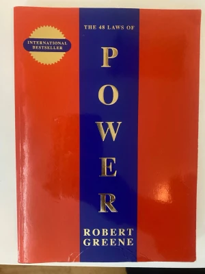The 48 Laws of Power bok - En ikonisk bok med röd och blå hårdpärm, guldtext och internationell bestseller-märke. Skriven av Robert Greene och känd för sina insikter om maktspel och strategi. Perfekt för dig som gillar psykologi och samhällsanalys.