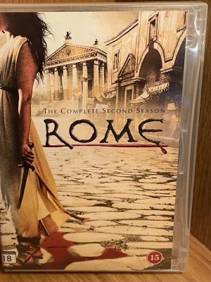 Rome Säsong 2 DVD-box - DVD-box med hela andra säsongen av serien Rome. Omslaget har motiv från antikens Rom med tempel och kullerstensgata, samt en person i antik klädsel. Boxen är i plast och innehåller flera skivor. Språk: svenska, engelska, finska, norska, danska. perfekt Skick