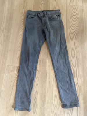 Grå smala jeans med detaljer - Snygga grå jeans i slim fit-modell med klassiska fem fickor och coola sömdetaljer på bakfickorna. Jeansen har bälteshällor och knappgylf. Materialet är mjukt denim som ger en skön känsla och passar perfekt till en avslappnad stil.