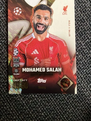 Två Topps fotbollssamlarbilder - Säljer två fotbollssamlarbilder från Topps med spelarna Mohamed Salah (Liverpool, röd tröja) och Serhou Guirassy (BVB, gul tröja). Korten har färgstarka tryck, klubbmärken och spelarstatistik. Perfekt för dig som gillar att samla på fotbollskort eller vill byta med vänner.