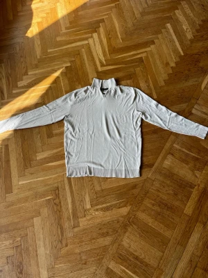 Beige stickad tröja med halvzip - Snygg beige stickad tröja från 157 med halvzip och hög krage. Tröjan har långa ärmar och ribbade muddar vid ärmslut och nederkant. Perfekt för lager på lager och enkel att matcha med olika outfits. Helt oanvänd 