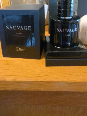 Dior Sauvage Elixir parfym - Dior Sauvage Elixir är en exklusiv parfym i en elegant, mörkblå glasflaska med silverdetaljer. Flaskan har en rund form och kommer i en matchande lyxig svart förpackning med tydlig logga. Doften är intensiv och maskulin, perfekt för dig som vill sticka ut. Obs jätte-lite använd - 95ml kvar. 