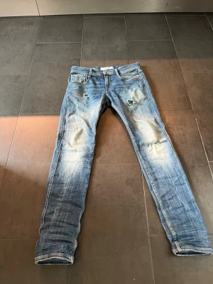 Ljusblå slitna skinny jeans - Säljer ett par ljusblå replay jeans med slitningar och hål på framsidan. Jeansen har klassisk femficksmodell, låg midja och är i ett mjukt denimtyg. Perfekta för en avslappnad och trendig look.storlek w29 L32