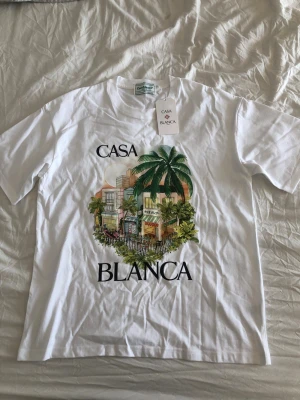 Casa Blanca t-shirt - Säljer en vit t-shirt från Casa Blanca med färgglatt tryck av palmer och byggnader. Helt ny och oanvänd. Storlek large. Pris kan diskuteras. 