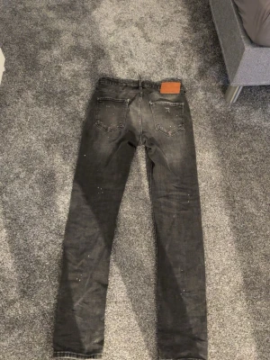 Svarta skinny jeans från Dsquared2 - Säljer ett par svarta skinny jeans från Dsquared2 i storlek 50. Jeansen har klassisk femficksmodell, läderpatch bak i midjan och diskreta slitningar för en cool look. Materialet är stretchigt denim som sitter snyggt och bekvämt.
