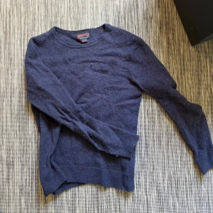 Mörkblå stickad tröja Superdry - Mysig mörkblå stickad tröja från Superdry med rund halsringning och ribbade muddar vid ärmslut och nederkant. Perfekt för lager på lager och enkel att matcha med jeans. Klassisk och stilren design .  Egentligen strl L, men krympt i tvätten så sitter som S. Hör av dig vid frågor// kan gå ner i pris vid snabb affär!😃/ Milton