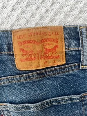 Levi's blå raka jeans - Klassiska blå jeans från Levi's med raka ben och femficksmodell. Jeansen har en tydlig läderpatch bak i midjan och den ikoniska röda Levi's-lappen på bakfickan. Tillverkade i slitstark denim med snygga kontrastsömmar. W30 L34
