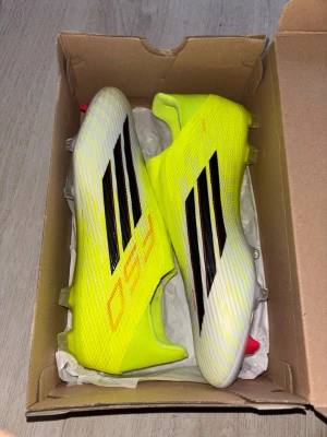 Gula Adidas fotbollsskor X 19+ - Säljer ett par grymma Adidas X 19+ fotbollsskor i neon-gult och vitt med svarta ränder. Skorna har en strumpliknande passform utan snörning och är tillverkade i lätt syntetmaterial. Sulan är delvis genomskinlig med röda dobbar för bästa grepp på planen.